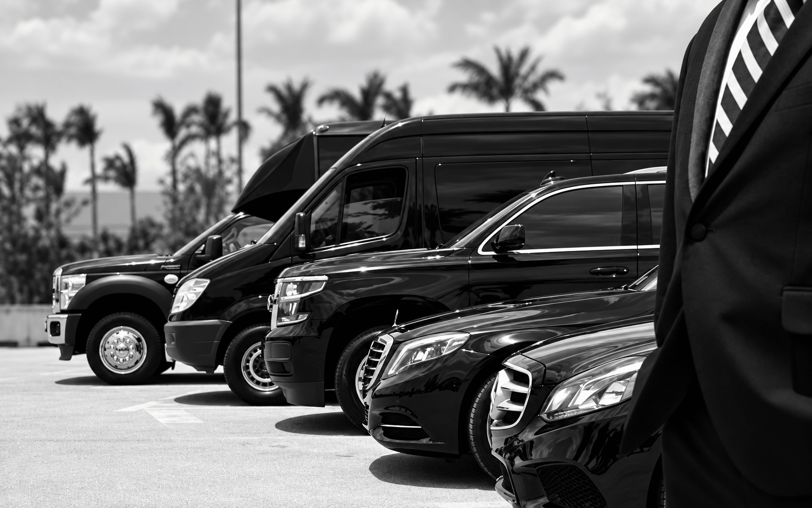Chauffeur beside a lineup of luxury sedans, an SUV, a passenger van and a bus